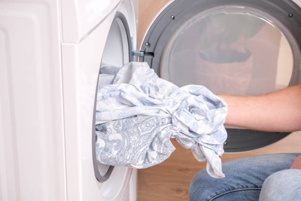 A man takes dried bed linen out of the dryer. Dryer machine in the house.